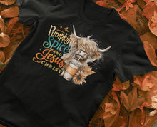 Load image into Gallery viewer, Black t-shirt with a graphic of a highland cow holding a pumpkin spice latte and text 'Pumpkin Spice and Jesus Christ' on a fall-themed background.
